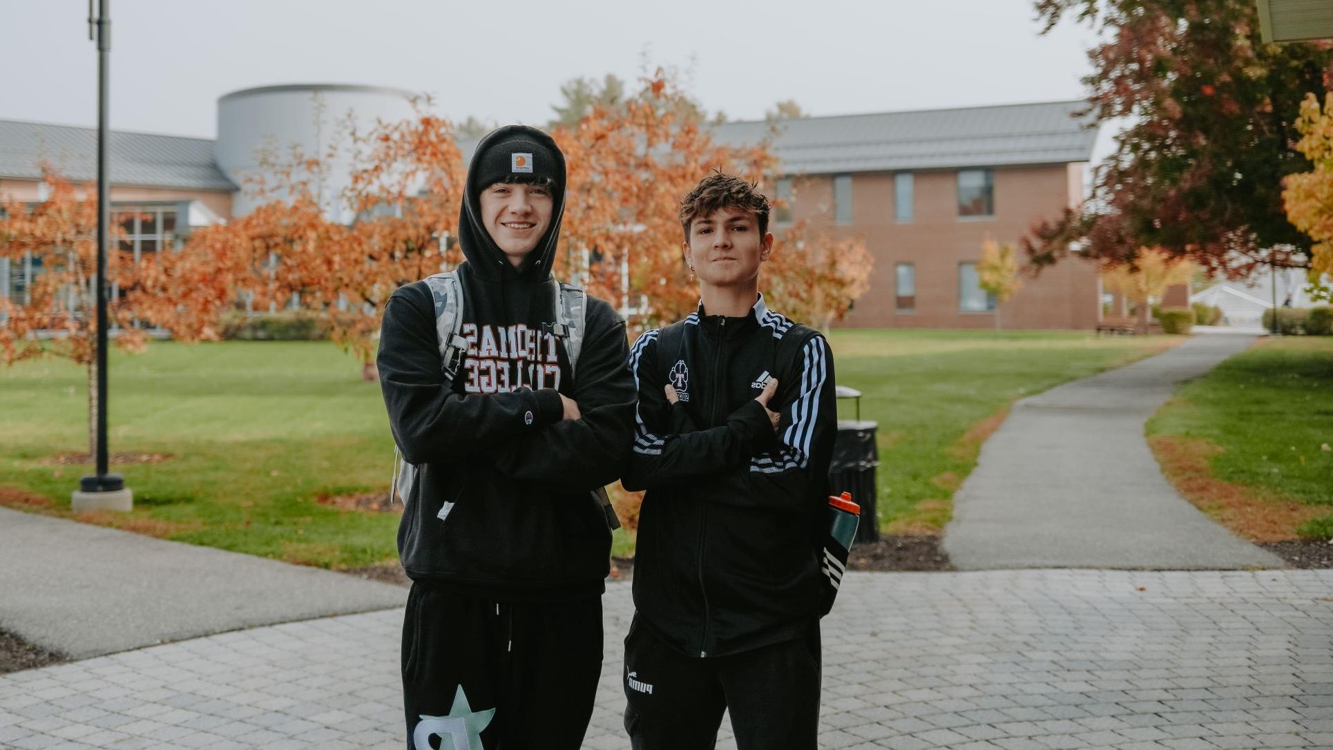 Two international students wearing 网上网赌平台大学 swag posed together with crossed arms on campus